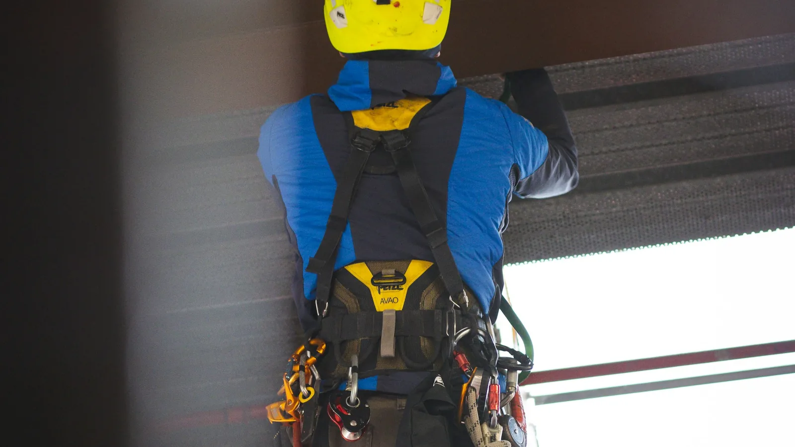 Worker in a hard hat and full-body harness working at height on a steel structure