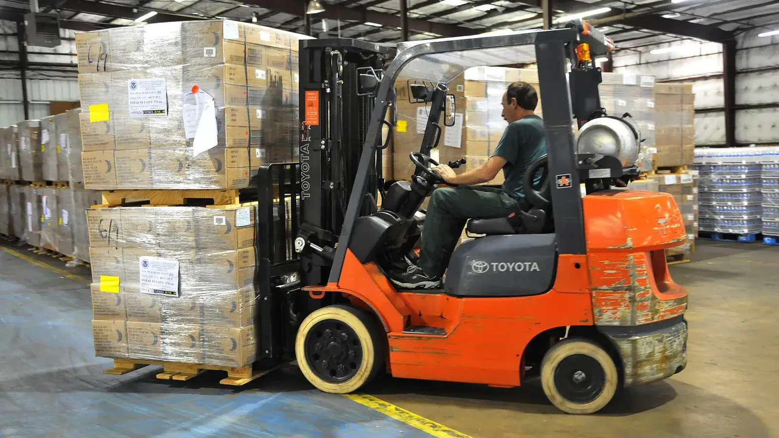 Operator driving a forklift with a pallet of boxed supplies through a warehouse