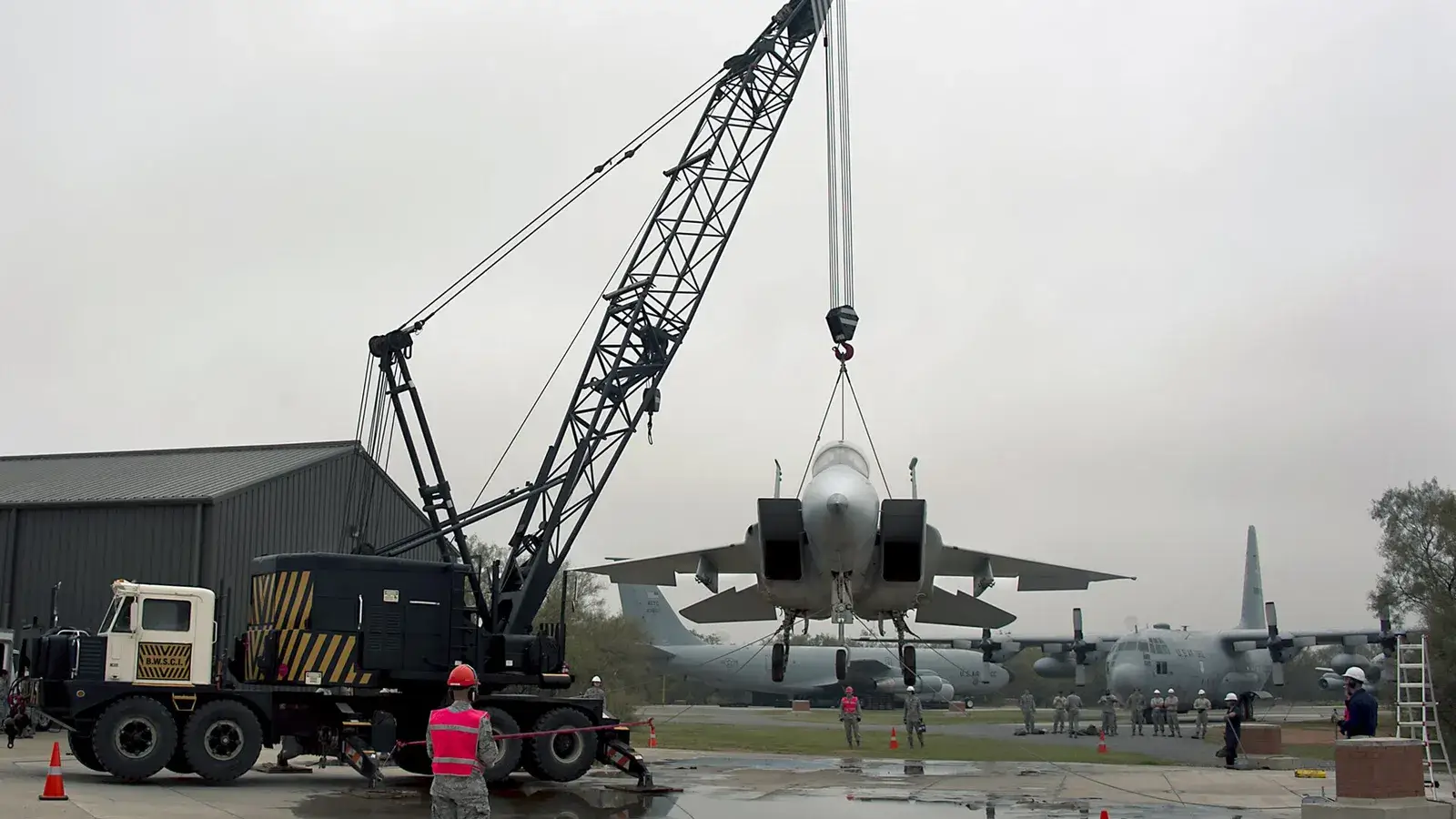 Crawler crane lifting a jet aircraft with slings while a rigger watches the load
