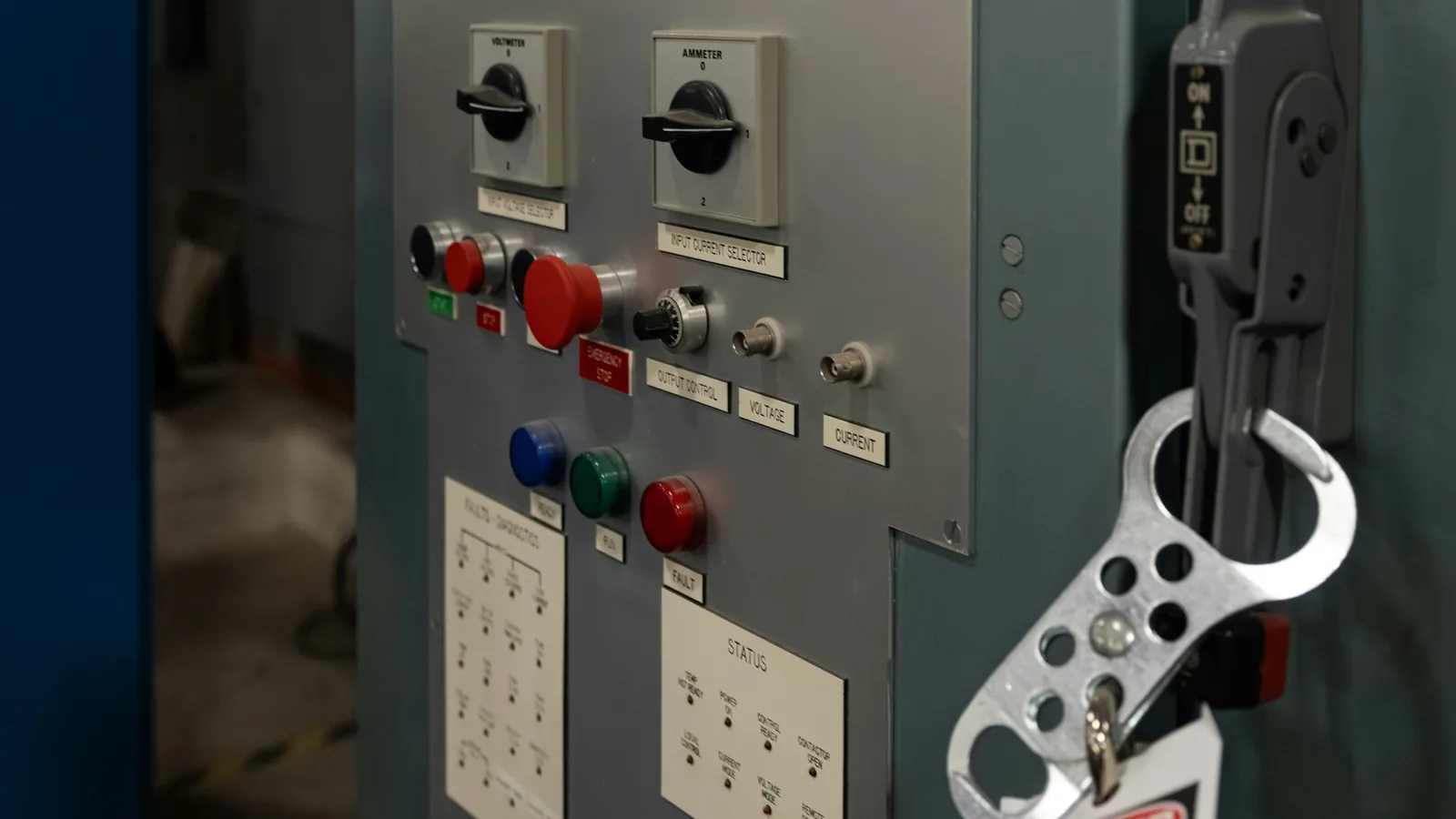 Lockout hasp hanging on an industrial control panel with switches and indicator lights