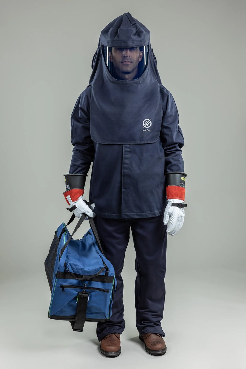 Worker wearing the Enespro ArcGuard 40 cal kit: navy FR coat, bib overall, and hood with face shield, holding the gear bag and wearing rubber insulating gloves