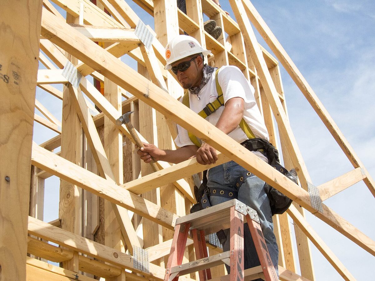 Roofer on residential framing wearing a harness tied to a fall arrest system